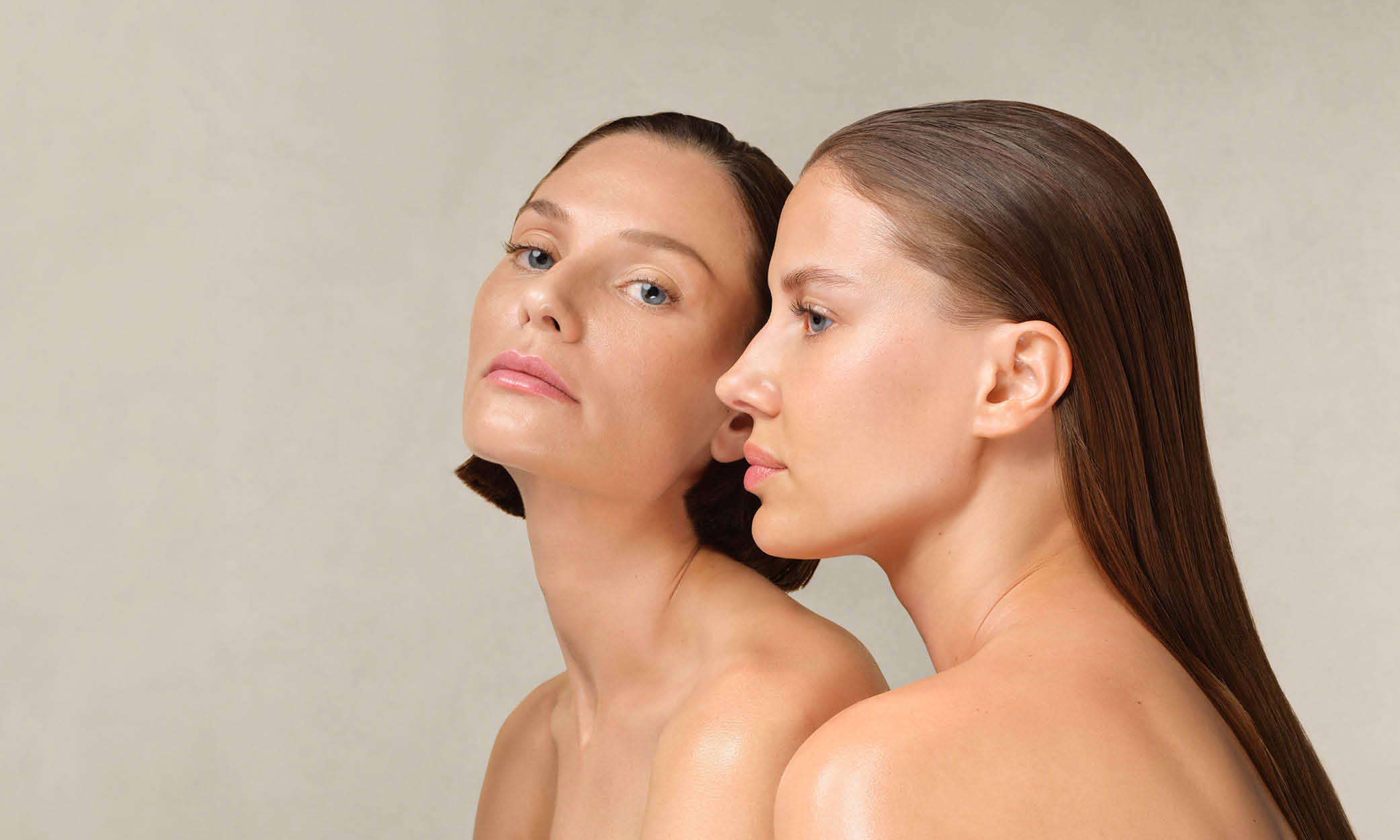 Zwei Frauen mit glatter Haut und zurückgekämmtem Haar, eine blickt frontal, die andere im Profil